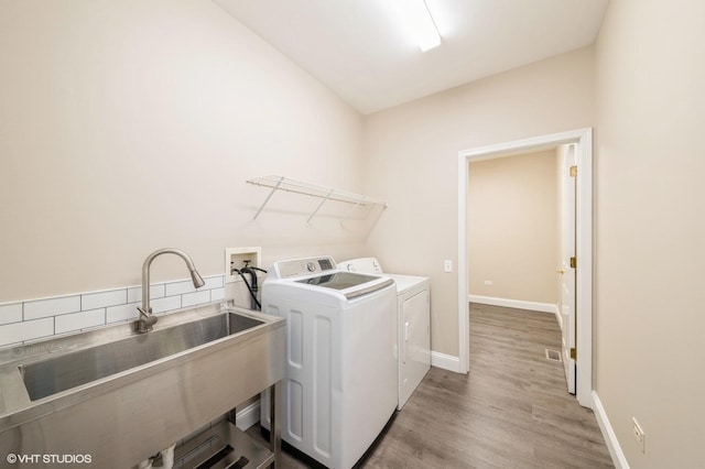 washroom with laundry area, baseboards, wood finished floors, washing machine and clothes dryer, and a sink