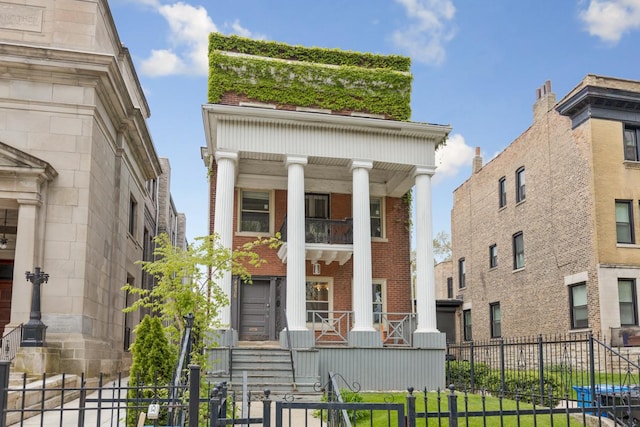 greek revival house featuring covered porch, brick siding, and a fenced front yard