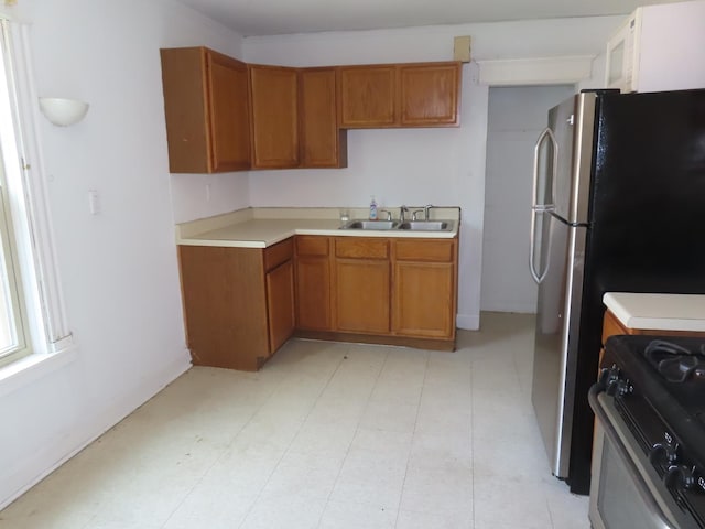 kitchen featuring a sink, light countertops, freestanding refrigerator, brown cabinets, and range with gas cooktop