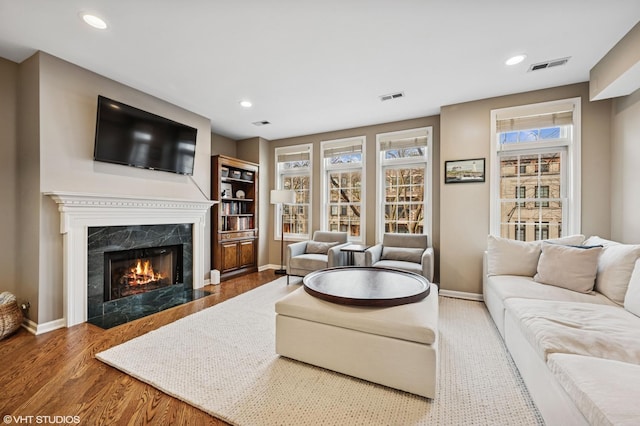 living room featuring wood finished floors, visible vents, baseboards, and a premium fireplace