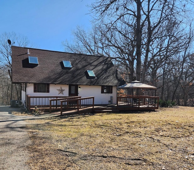 rear view of property with a gazebo, roof with shingles, and a wooden deck