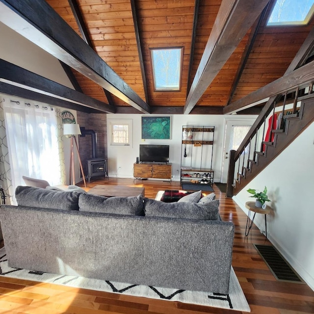 living room featuring visible vents, lofted ceiling with skylight, wood finished floors, a wood stove, and stairs