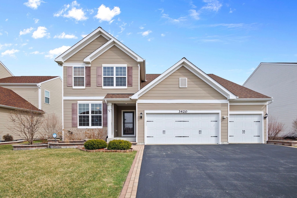 traditional home featuring aphalt driveway, a garage, and a front lawn