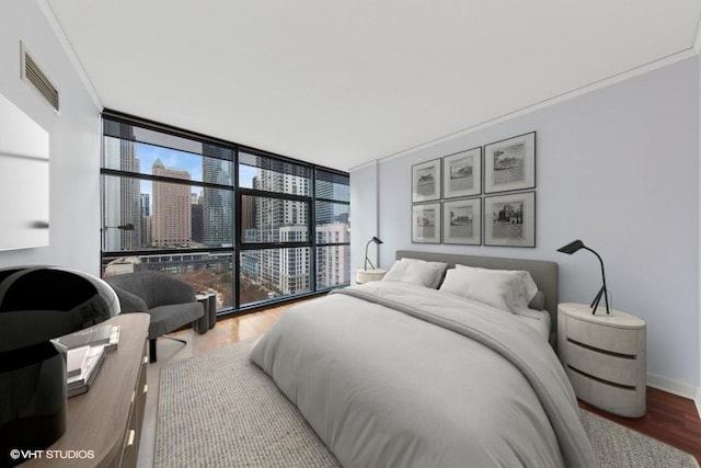 bedroom with baseboards, visible vents, wood finished floors, a view of city, and floor to ceiling windows