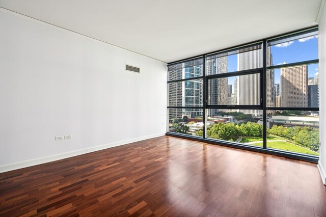 spare room featuring visible vents, baseboards, wood finished floors, a city view, and floor to ceiling windows