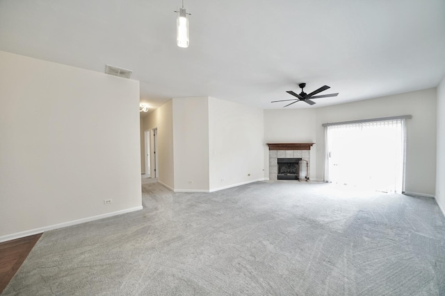 unfurnished living room with carpet, a tiled fireplace, a ceiling fan, and baseboards