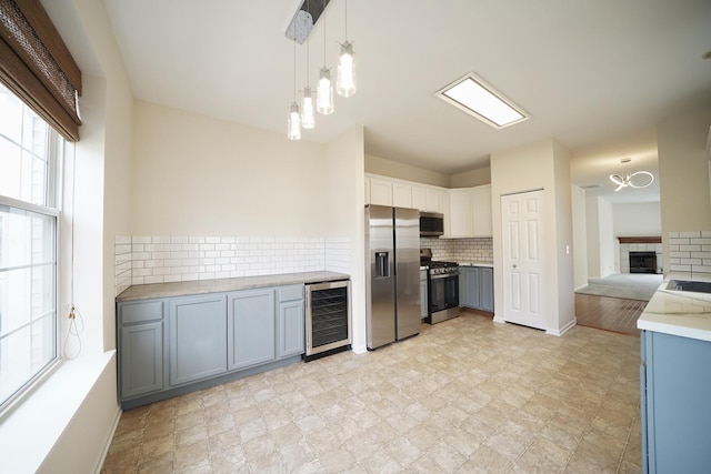 kitchen featuring beverage cooler, decorative backsplash, stainless steel appliances, light countertops, and a fireplace