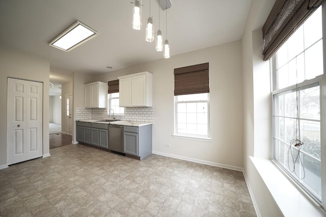 kitchen featuring a sink, baseboards, light countertops, stainless steel dishwasher, and backsplash