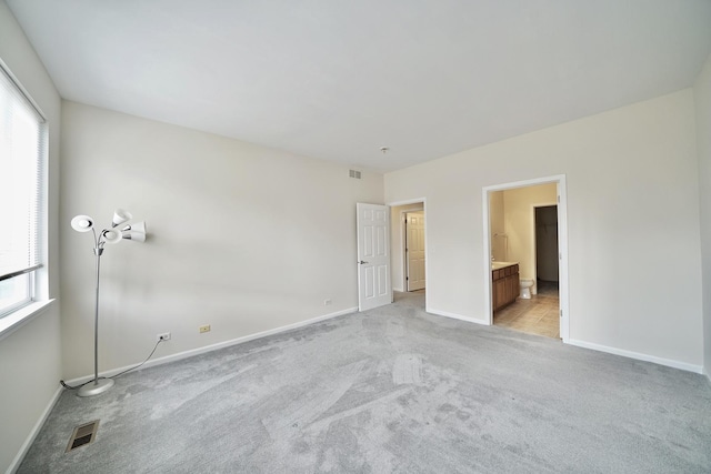 unfurnished bedroom featuring light colored carpet, visible vents, baseboards, and ensuite bathroom