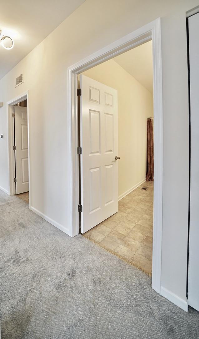 hall featuring carpet floors, visible vents, and baseboards