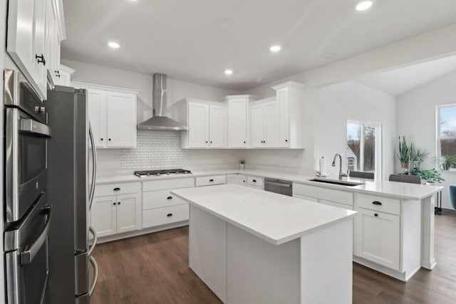 kitchen with stainless steel appliances, light countertops, a sink, wall chimney range hood, and a peninsula