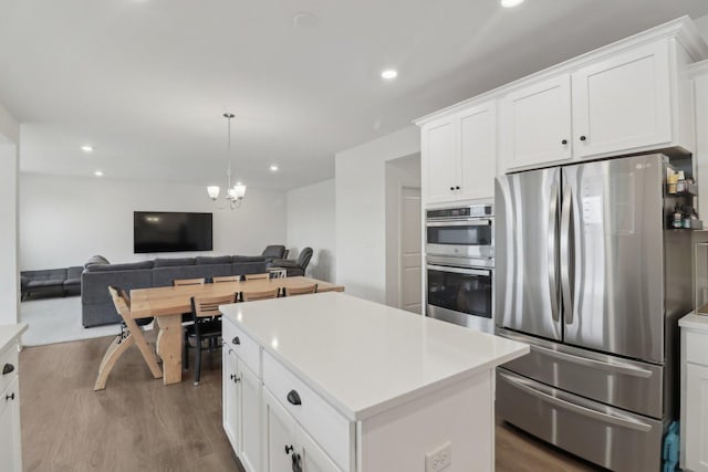 kitchen with white cabinets, a kitchen island, open floor plan, wood finished floors, and stainless steel appliances