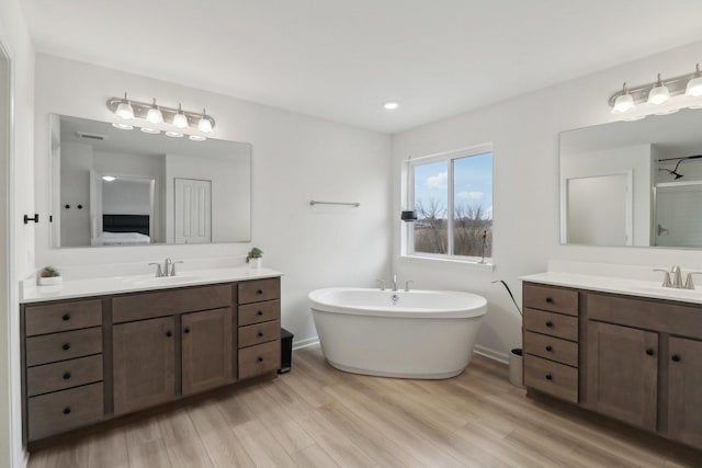 full bathroom with two vanities, a sink, a freestanding bath, and wood finished floors