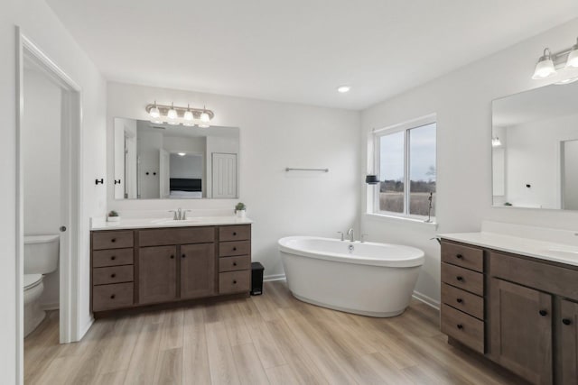 full bath with a freestanding tub, a sink, toilet, and wood finished floors