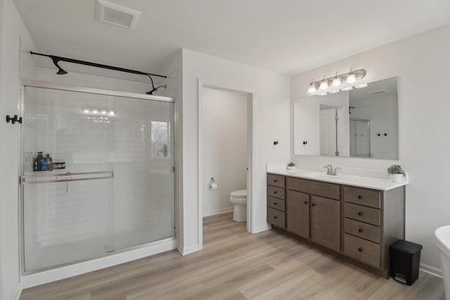 bathroom featuring visible vents, toilet, a stall shower, vanity, and wood finished floors