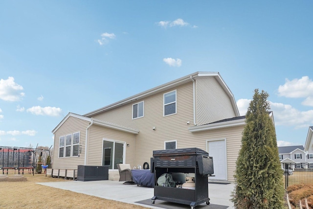 rear view of house featuring a patio area, a trampoline, and fence