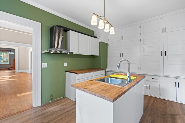 kitchen with white cabinets, dark wood-style floors, butcher block counters, wall chimney exhaust hood, and a sink