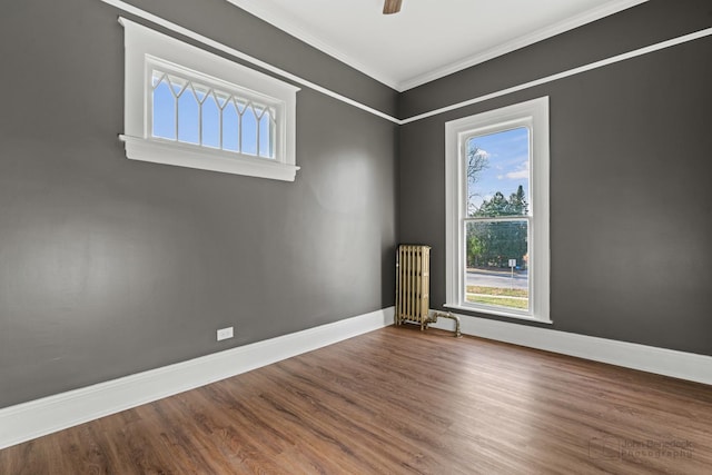 empty room with crown molding, radiator heating unit, ceiling fan, wood finished floors, and baseboards