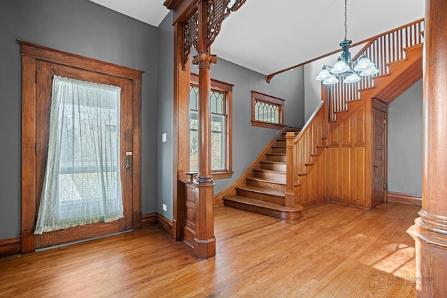 entryway featuring a notable chandelier, wood finished floors, baseboards, stairs, and ornate columns