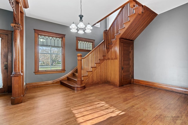 stairs with a notable chandelier, wood finished floors, decorative columns, and baseboards