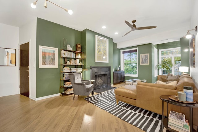 living area with baseboards, a ceiling fan, a fireplace with flush hearth, wood finished floors, and recessed lighting