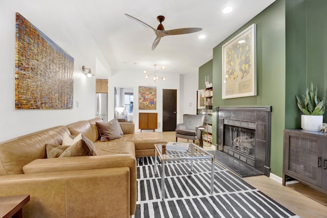 living room with recessed lighting, ceiling fan with notable chandelier, wood finished floors, a high end fireplace, and baseboards