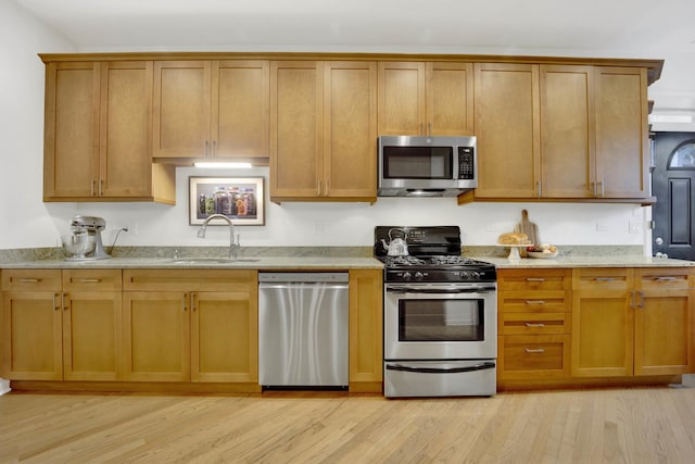 kitchen featuring light wood-style flooring, appliances with stainless steel finishes, brown cabinets, light stone counters, and a sink