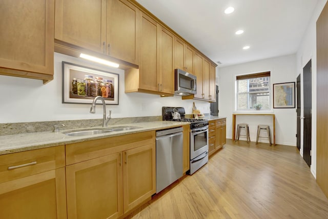 kitchen featuring recessed lighting, stainless steel appliances, a sink, light wood-type flooring, and light stone countertops