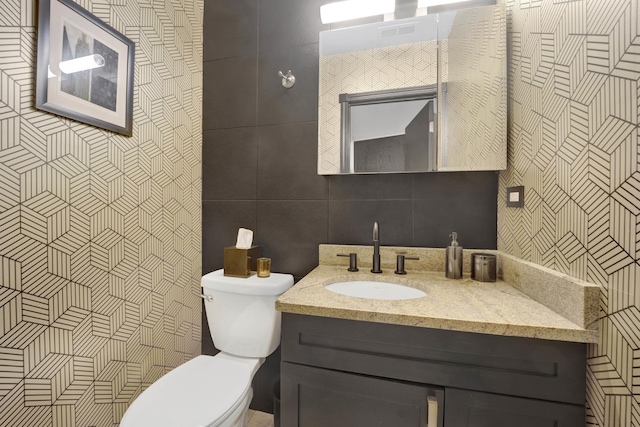 bathroom with toilet, tile walls, and vanity