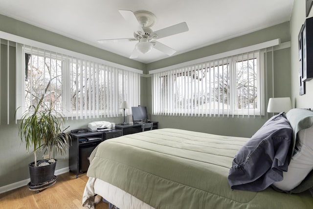 bedroom featuring a ceiling fan, multiple windows, baseboards, and wood finished floors