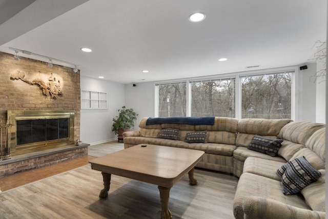 living area featuring baseboards, wood finished floors, a brick fireplace, track lighting, and recessed lighting