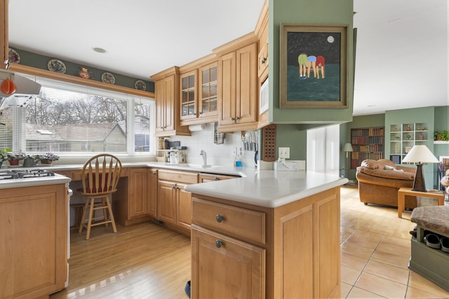 kitchen with glass insert cabinets, open floor plan, a peninsula, light countertops, and a sink