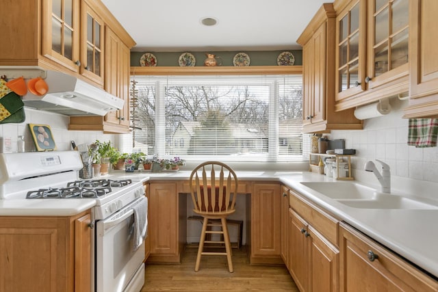 kitchen featuring under cabinet range hood, a sink, light wood-style floors, light countertops, and white gas range