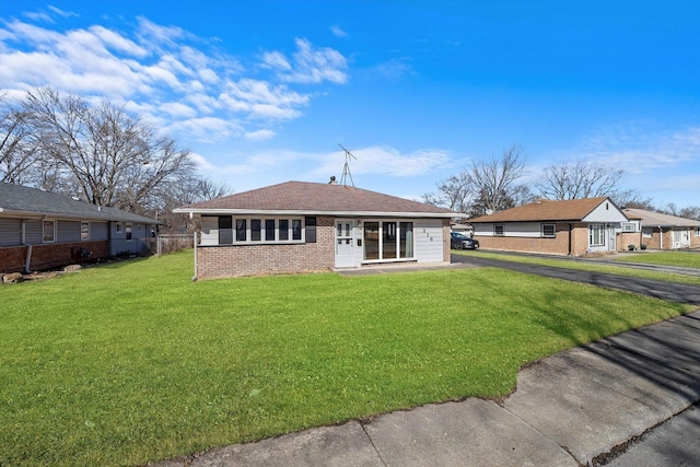 rear view of property with driveway, brick siding, and a lawn