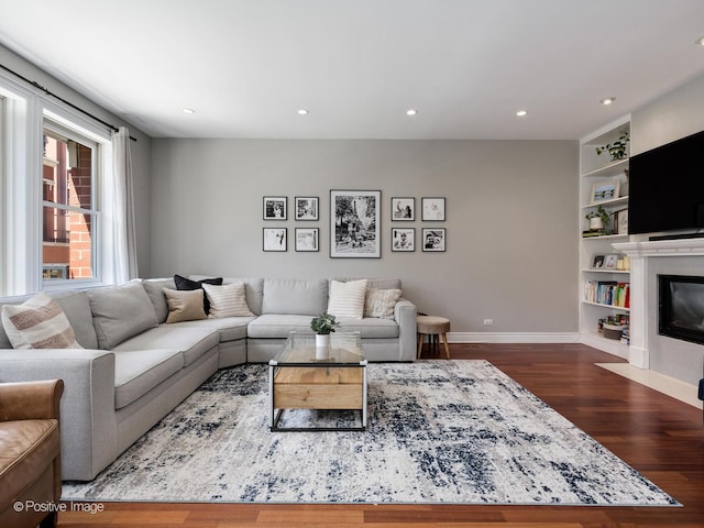 living room featuring built in features, dark wood-style flooring, baseboards, and a fireplace with flush hearth