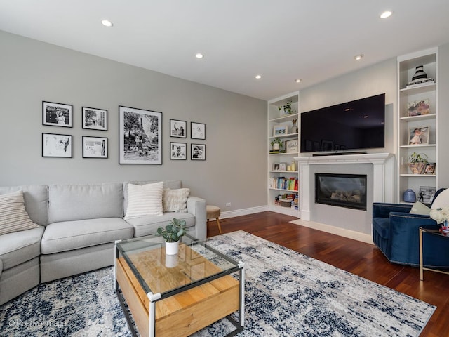 living area with dark wood-style floors, built in shelves, baseboards, and a glass covered fireplace