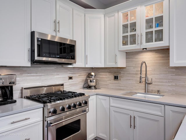 kitchen featuring light countertops, backsplash, appliances with stainless steel finishes, white cabinets, and a sink