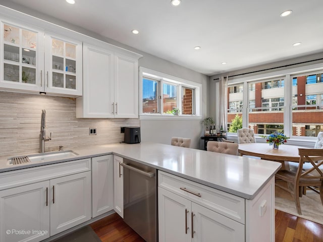 kitchen with a peninsula, a sink, white cabinets, backsplash, and dishwasher