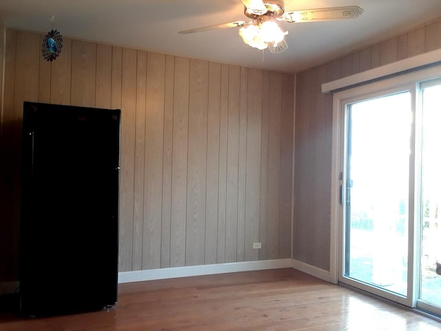 spare room with wooden walls, a ceiling fan, light wood-style flooring, and baseboards