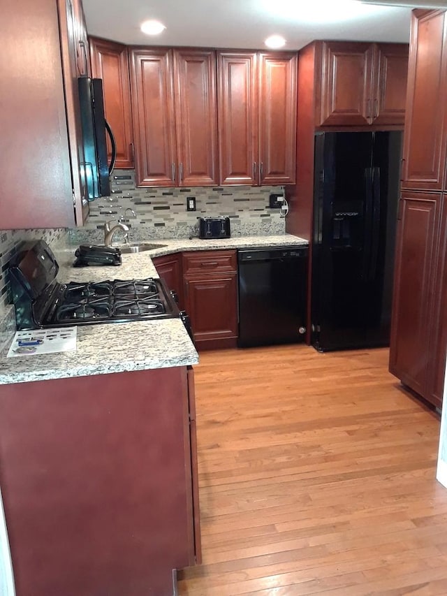 kitchen with light wood-type flooring, black appliances, tasteful backsplash, and a sink