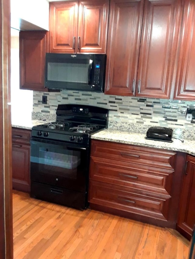 kitchen with black appliances, light wood finished floors, backsplash, and light stone countertops