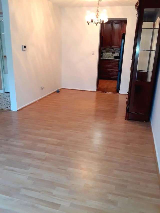 unfurnished dining area featuring baseboards, a notable chandelier, and light wood finished floors