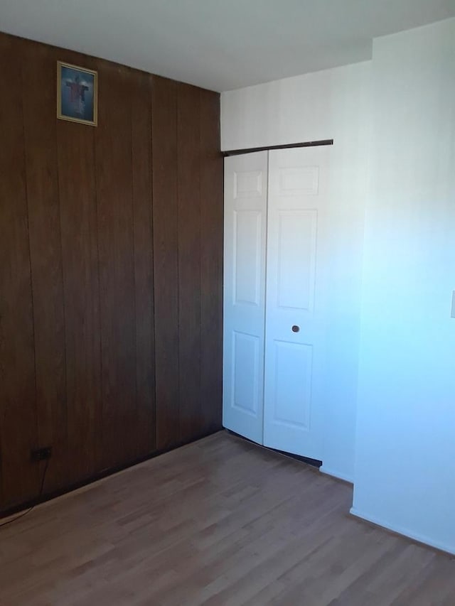 unfurnished bedroom with wood finished floors, wooden walls, and a closet