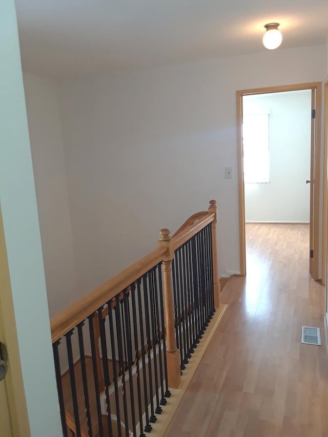 hall with light wood-style flooring, visible vents, and an upstairs landing