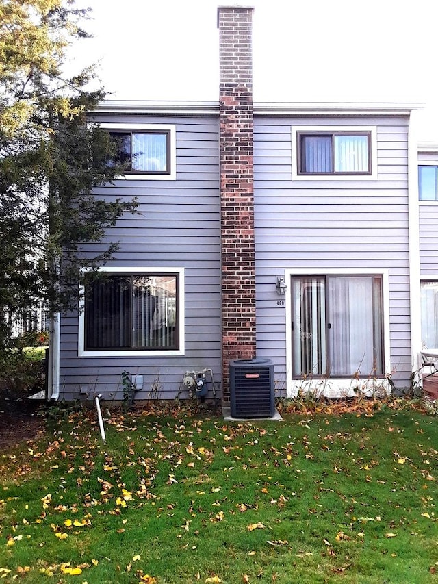 back of property with central AC, a lawn, and a chimney