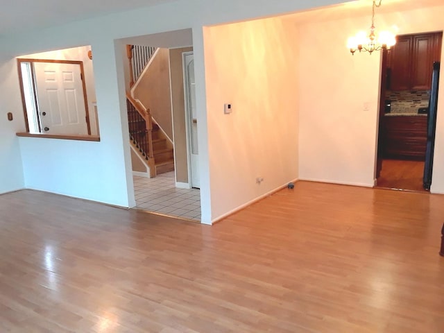 unfurnished room featuring light wood finished floors, baseboards, an inviting chandelier, and stairs
