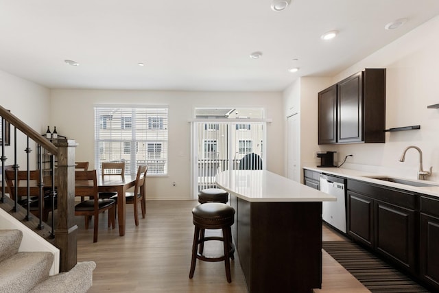 kitchen featuring a breakfast bar, a sink, light wood-style floors, light countertops, and stainless steel dishwasher