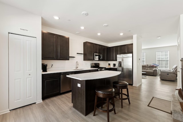 kitchen with appliances with stainless steel finishes, open floor plan, light countertops, dark brown cabinets, and a sink