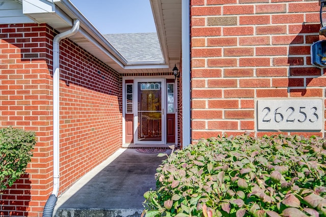 doorway to property featuring brick siding and roof with shingles