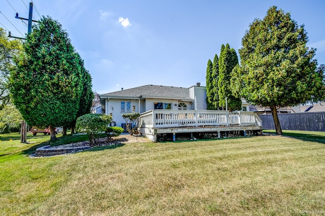 rear view of house with a lawn, a wooden deck, and fence